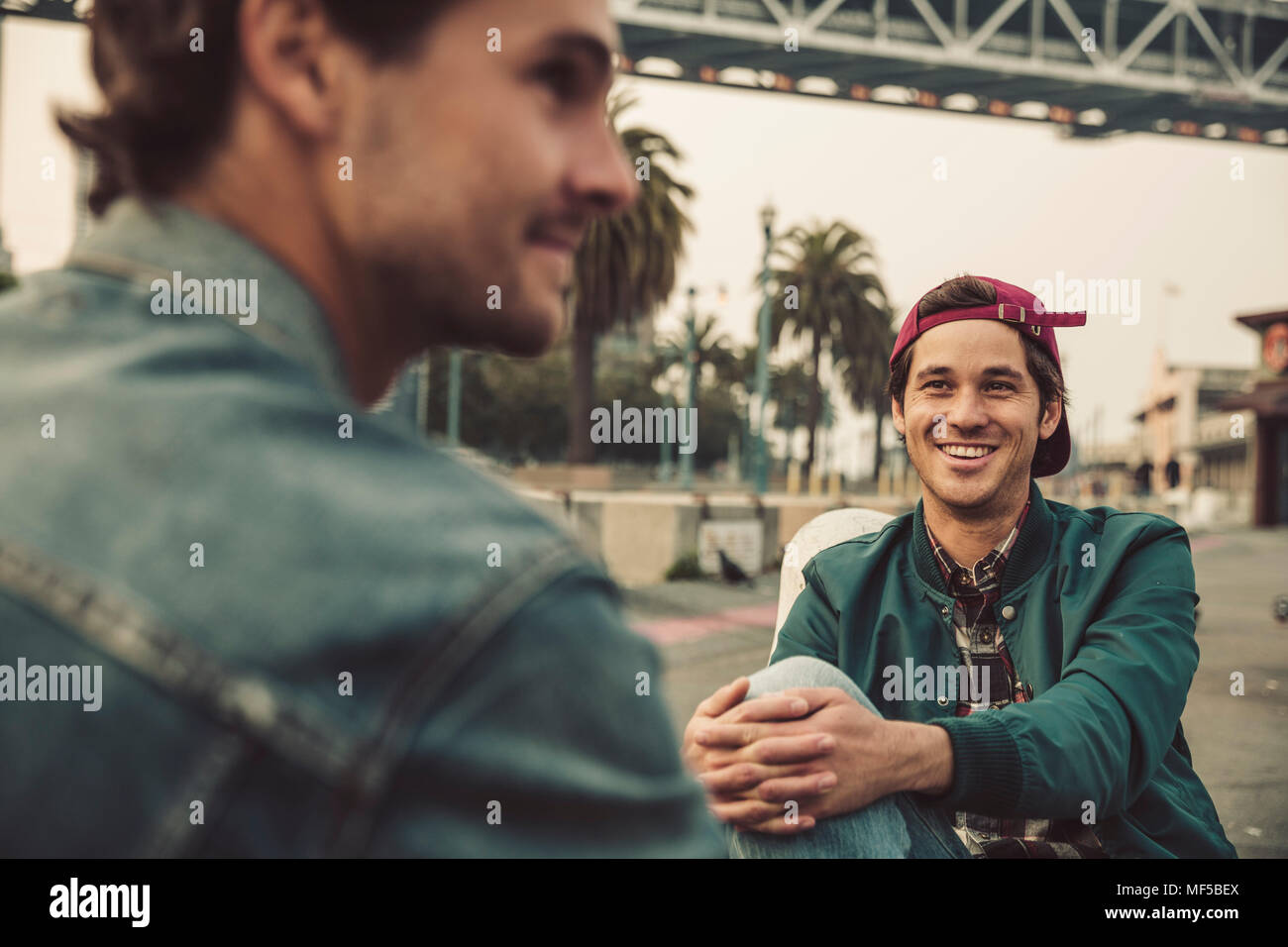 Zwei lächelnde junge Männer sitzen im Freien sprechen Stockfoto