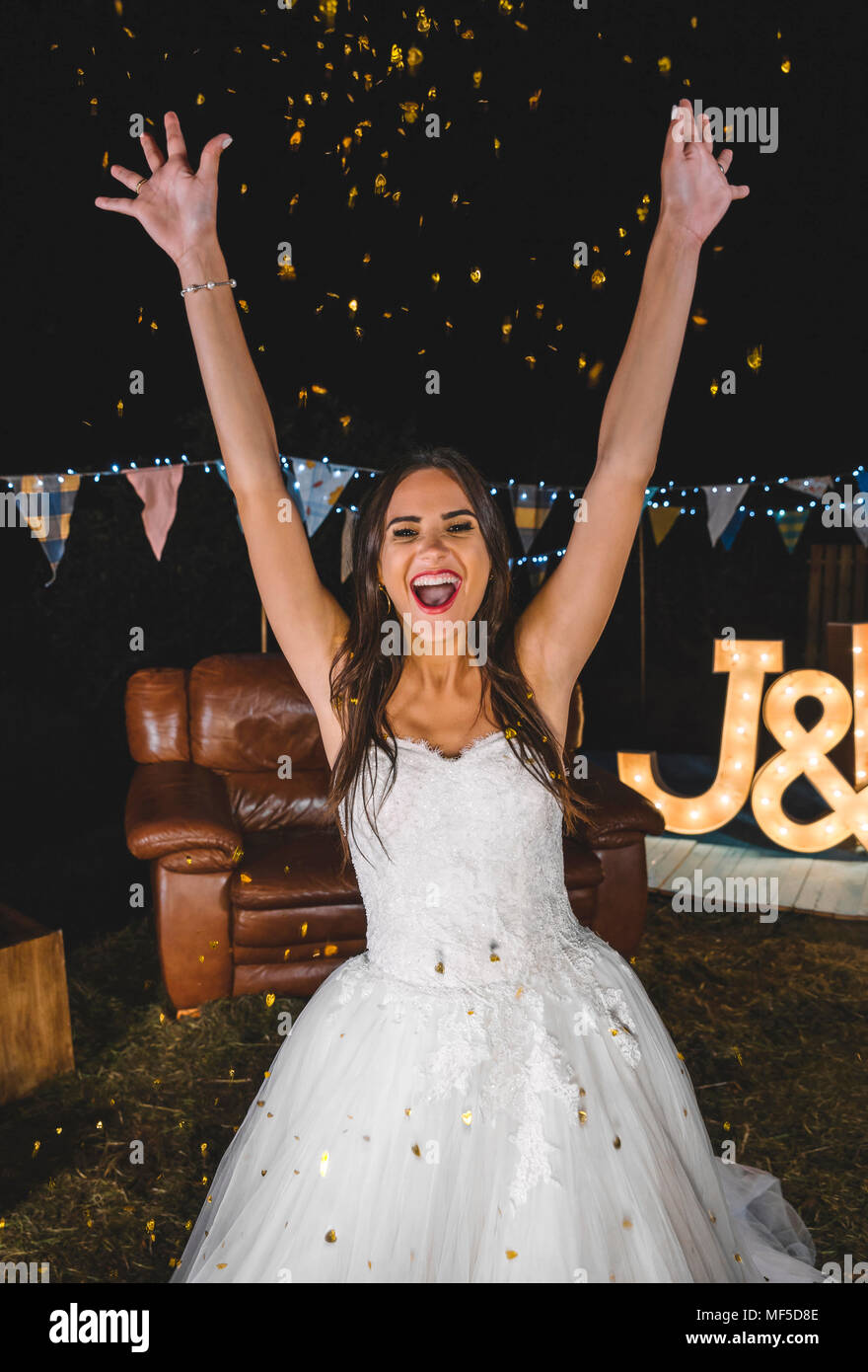 Fröhliche Braut heben ihre Arme während Konfetti über sie fallen auf eine Nacht im Freien Stockfoto