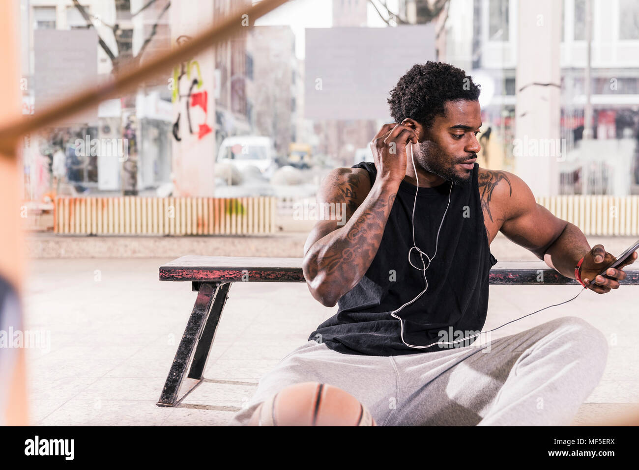 Mann mit Tattoos und Sie ihr Smartphone- und Ohrhörer Basketball Stockfoto
