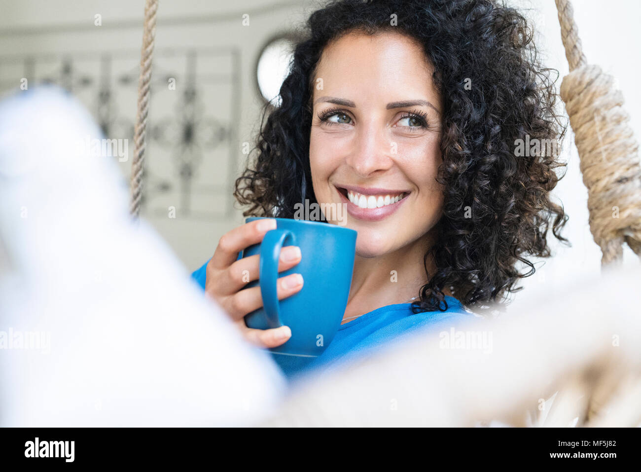 Lächelnde Frau mit lockigem Haar holding Tasse Kaffee Stockfoto