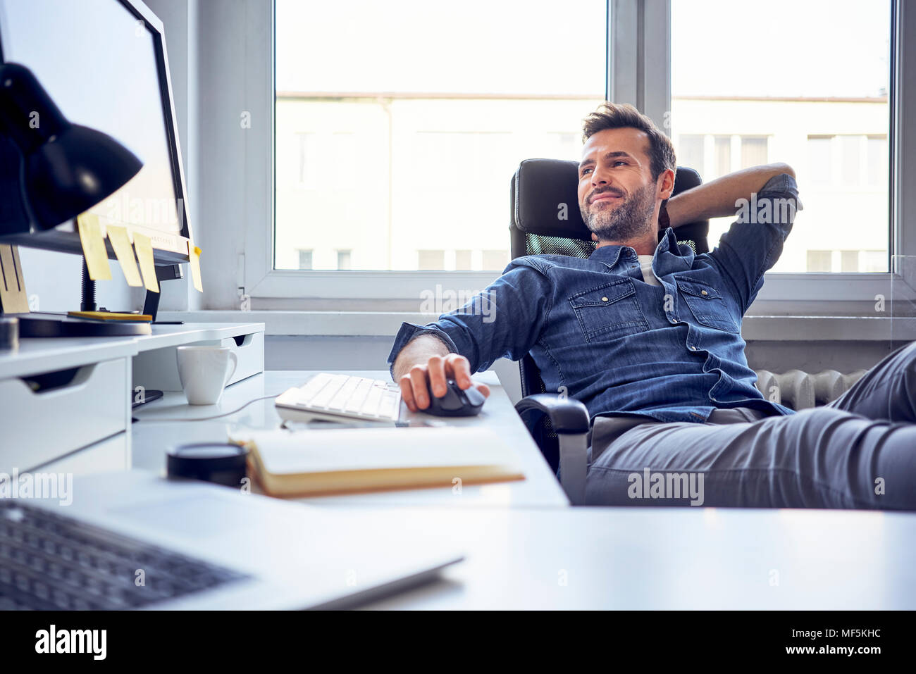 Entspannt Mann sitzt am Schreibtisch im Büro auf dem Bildschirm Stockfoto