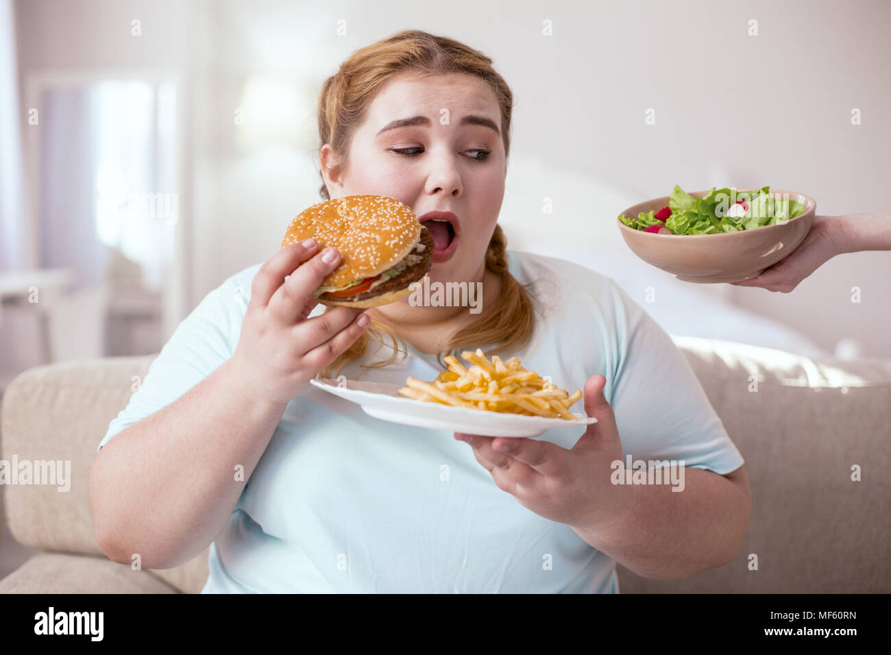 Mollige junge Frau denken über ihre ungesunde Essgewohnheiten Stockfoto