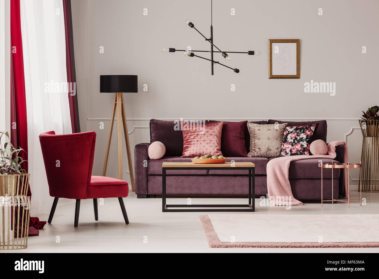 Roten Sessel in der Nähe von Holz- Tisch und lila Sofa gegen die Wand mit Mockup in Wohnzimmer Innenraum Stockfoto