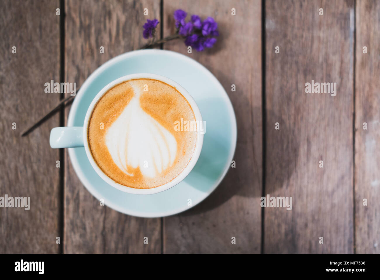 Blick von oben auf die heißen Kaffee in grün Tasse mit Latte Art auf Holzbrett Tabelle mit vergessen mich nicht Blumen, Essen und Trinken Konzept, vintage Filter Stockfoto