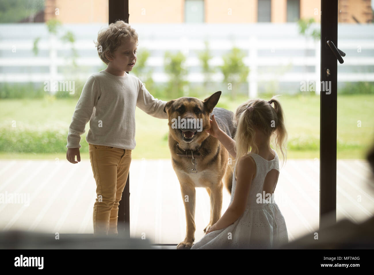 Kinder, Junge und Mädchen spielen mit Hund kommen im Haus Stockfoto