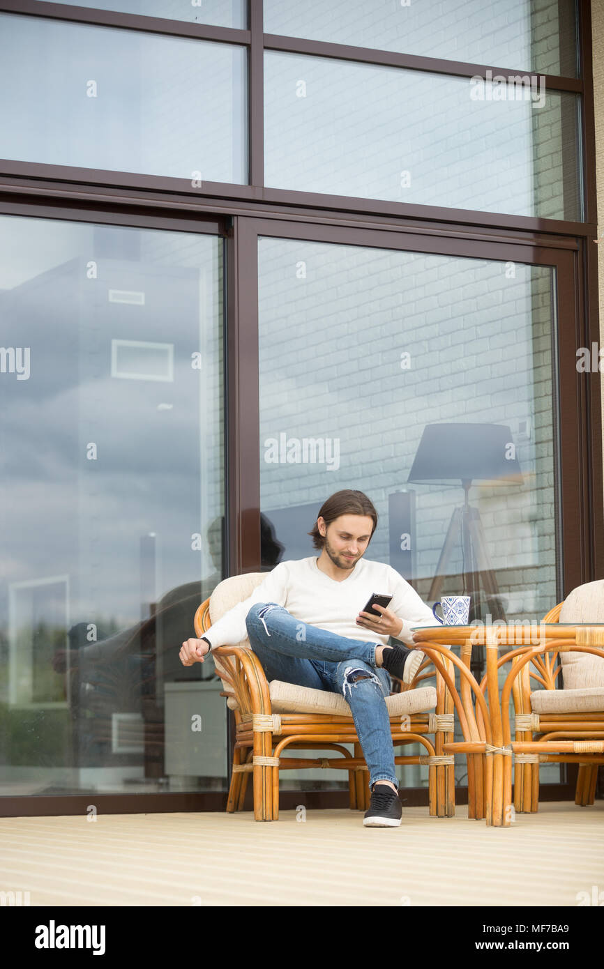 Entspannt man mit Smartphone sitzt außen am Haus Terrasse ch Stockfoto