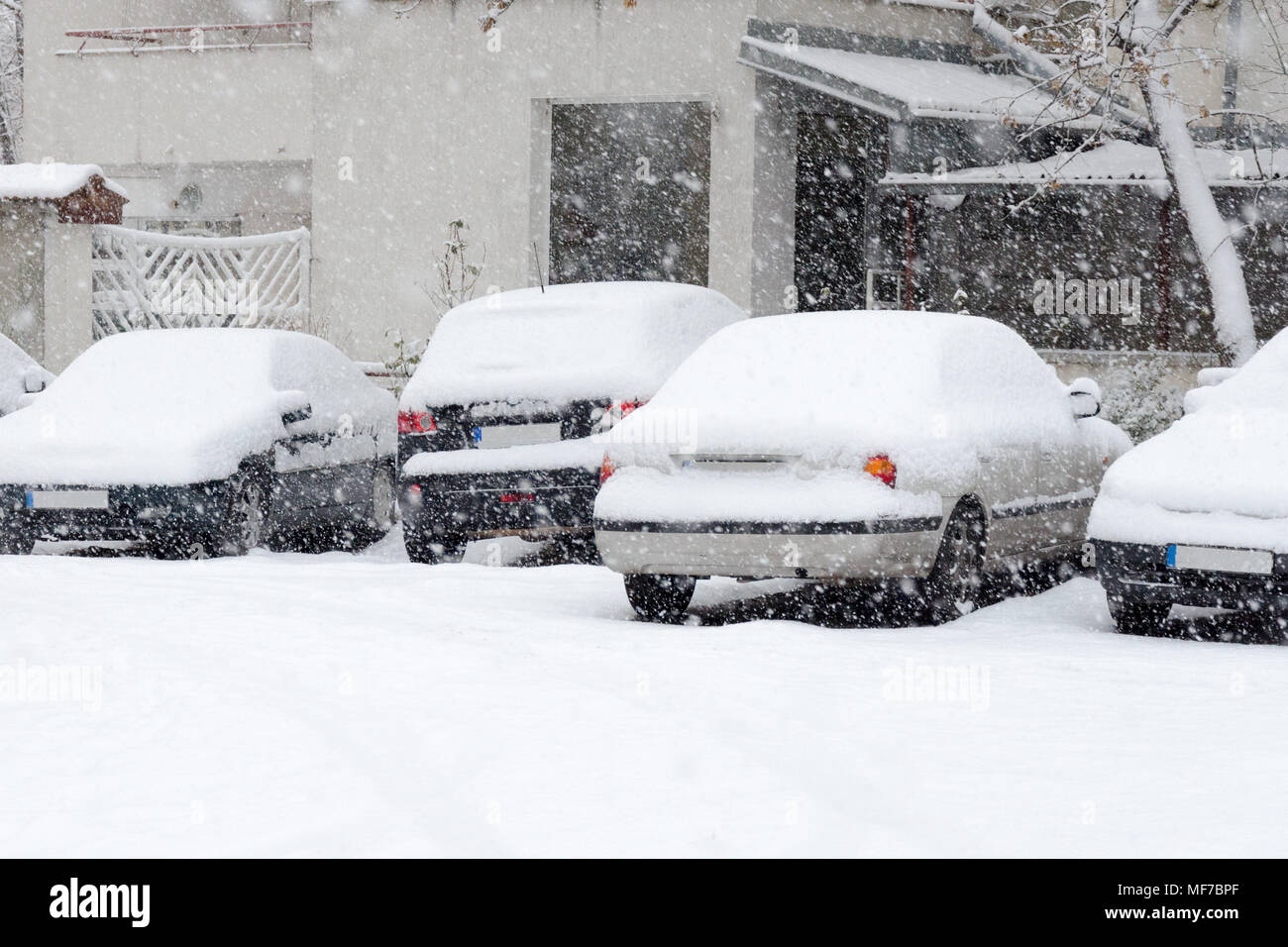 Rückseite der geparkten Autos mit Schnee bedeckt, während schneite, weißes Gebäude im Hintergrund Stockfoto