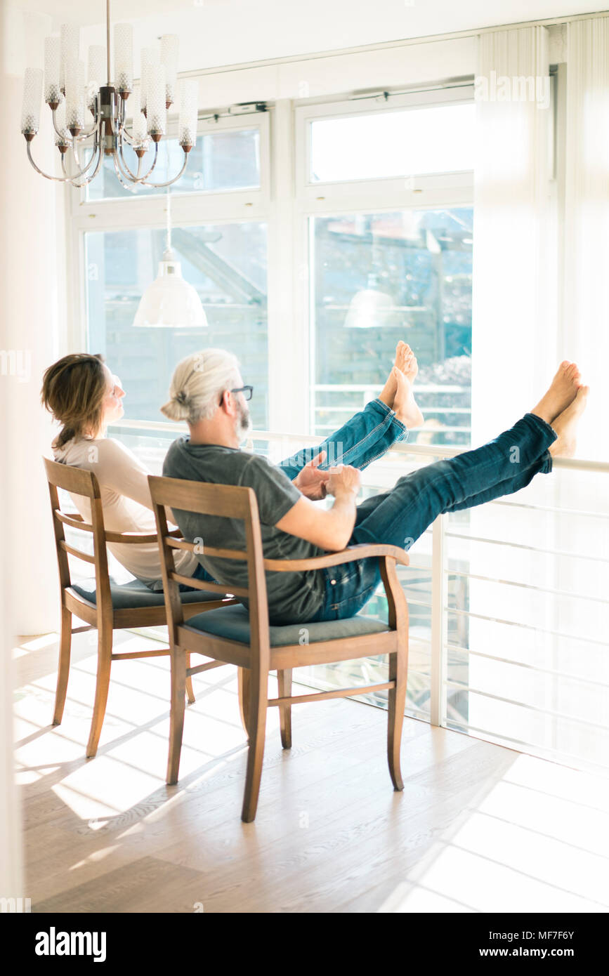 Entspannt reifes Paar zu Hause sitzen auf Stühlen mit Füßen bis Stockfoto