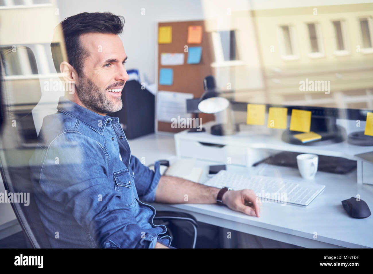 Lächelnd Mann schaut durch das Fenster im Büro am Schreibtisch sitzen Stockfoto