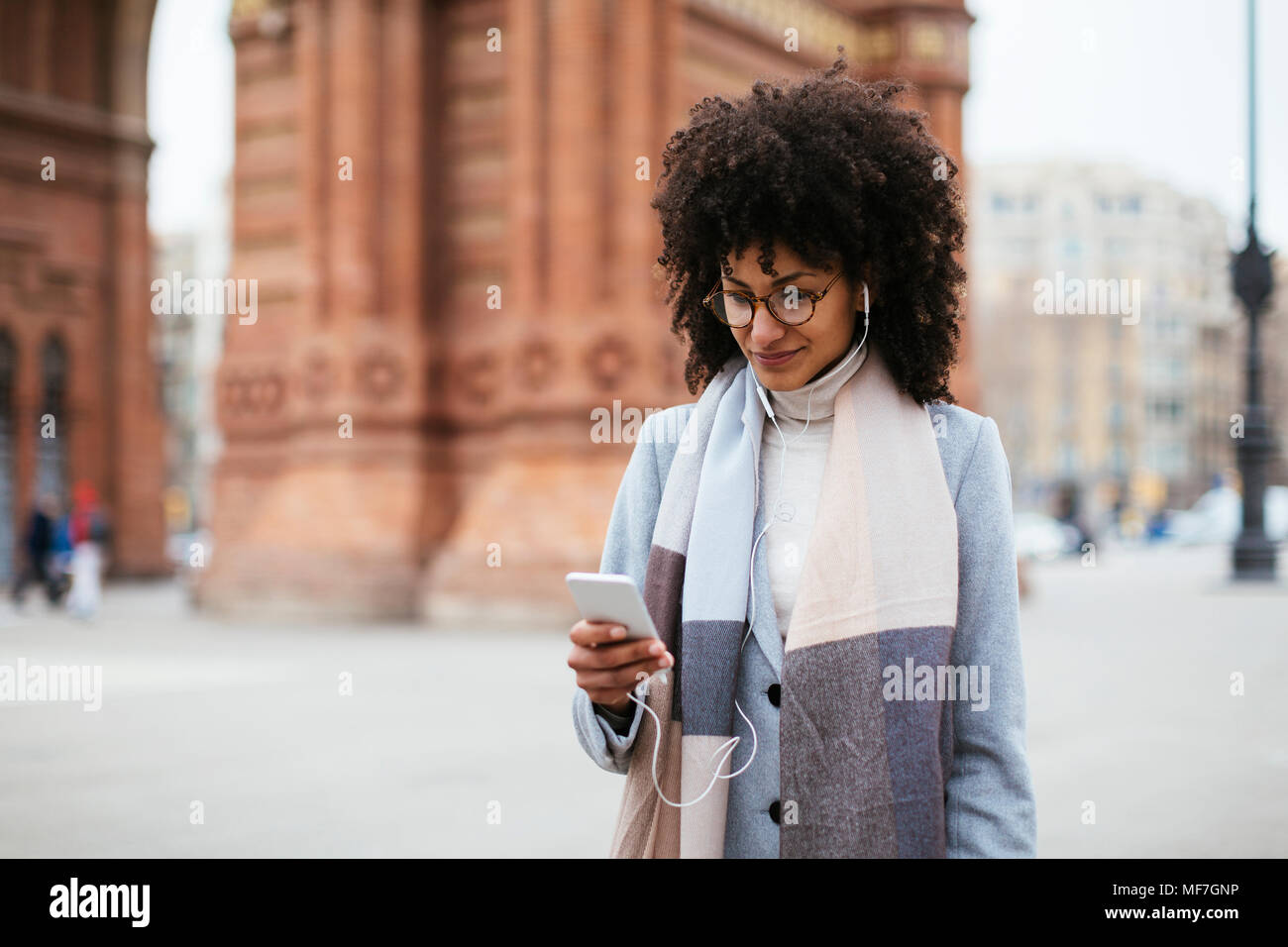 Spanien, Barcelona, lächelnde Frau mit Handy- und Ohrhörer in der Stadt Stockfoto