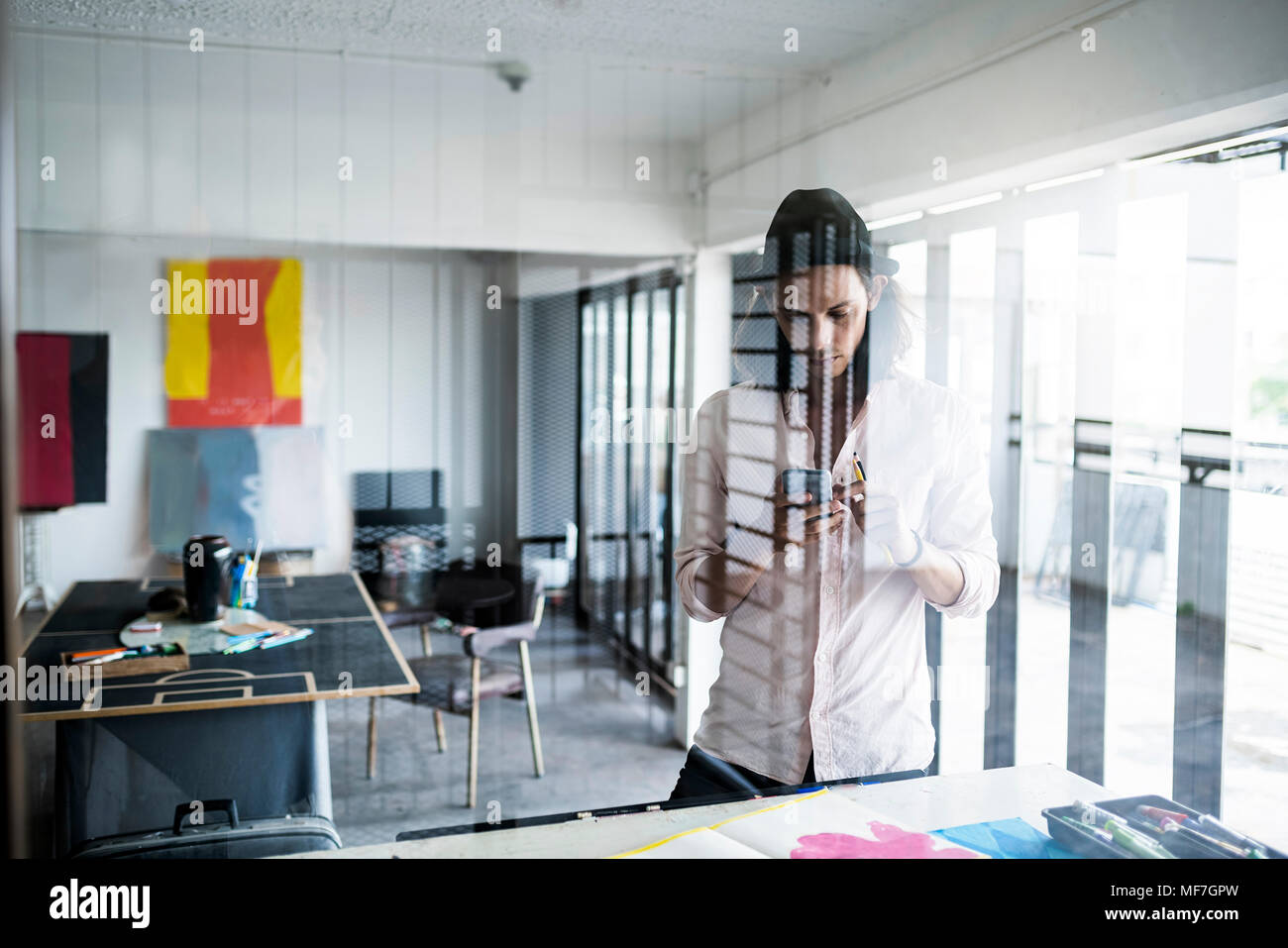 Junge Künstler bei der Arbeit in seinem Loft Studio unter Smartphone Bild von seinem Kunstwerk. Stockfoto