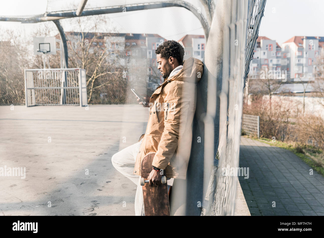 Junger Mann mit Skateboard auf Gericht prüfen Smartphone Stockfoto