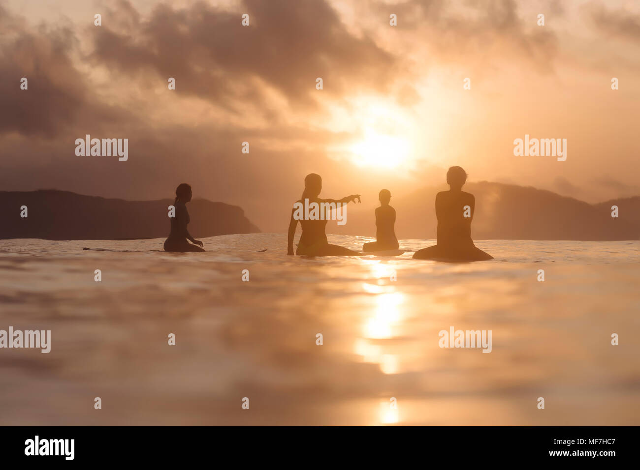 Indonesien, Lombok, Gruppe von Surfern auf Surfboards bei Sonnenuntergang sitzen Stockfoto