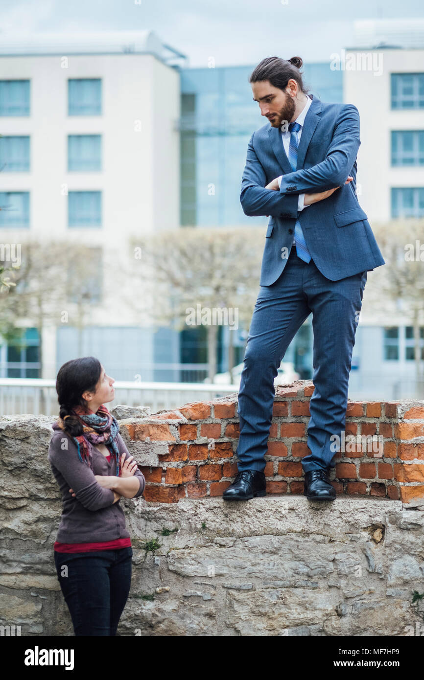 Geschäftsmann steht auf einer Mauer auf Frau Stockfoto