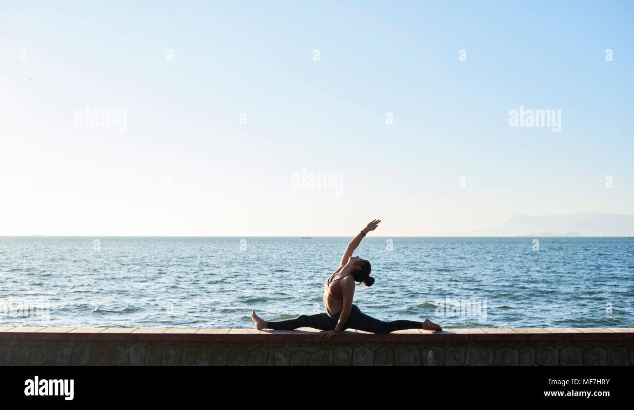 Junge Frau mit Yoga an der Wand durch das Meer Stockfoto