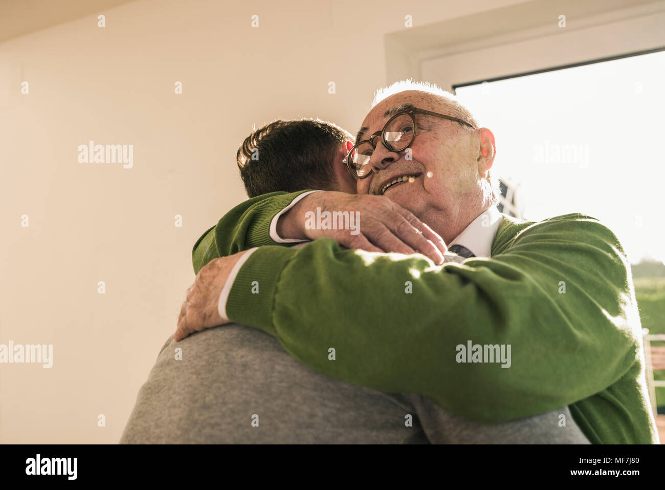 Lächelnd älterer Mann umarmt jungen Mann Stockfoto