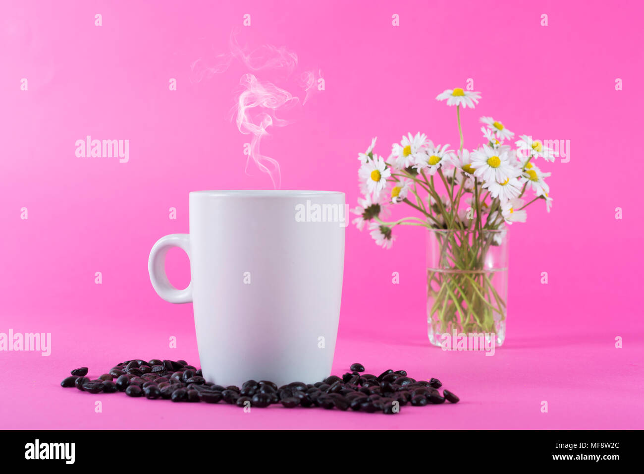 Tasse Kaffee mit Rauch und Kaffeebohnen und verschwommenes daisy flowers im Hintergrund, im Studio Stockfoto