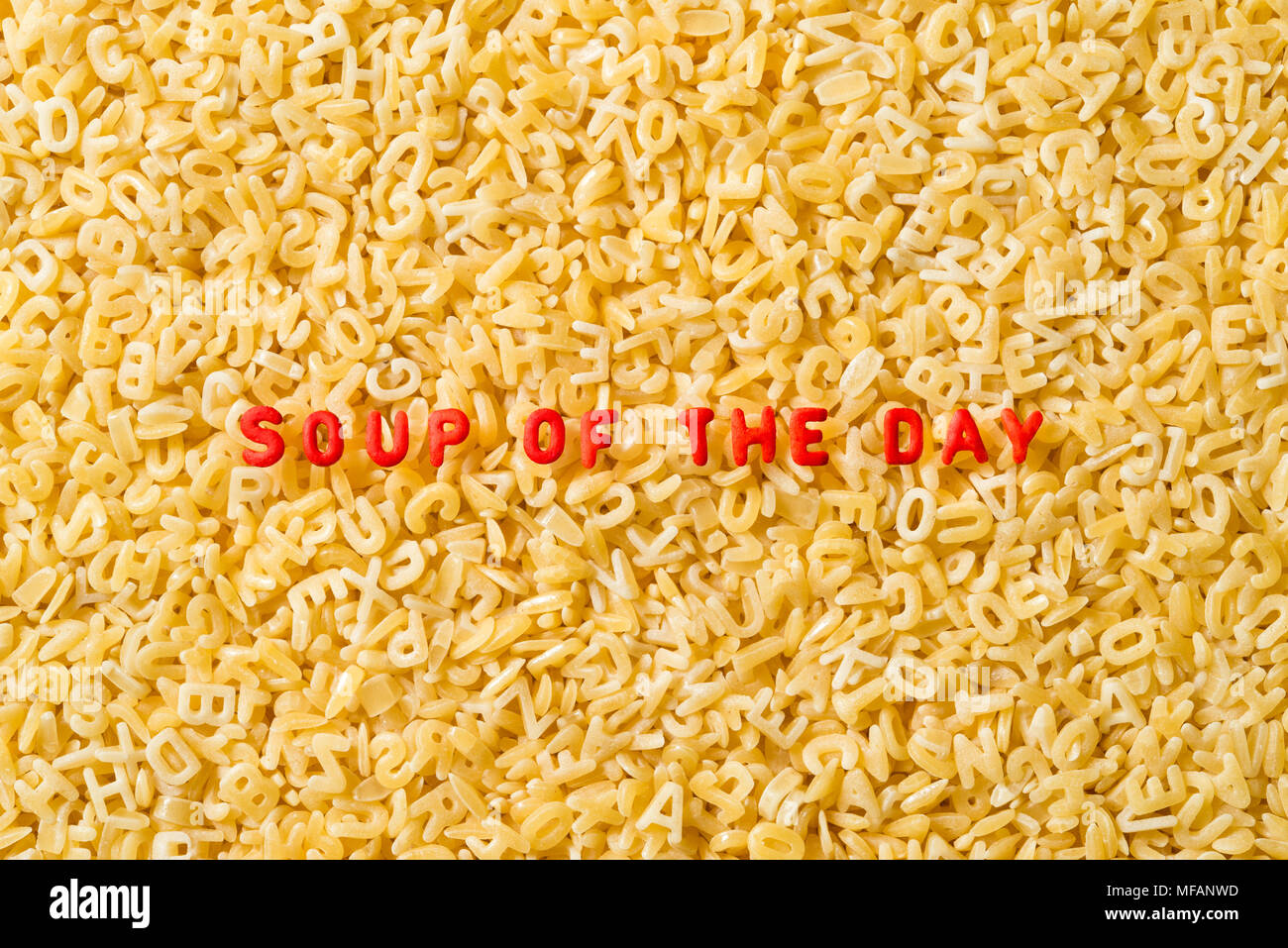 Die Worte "soup of the Day" sind mit rot gefärbten ABC-Nudelbuchstaben geschrieben. Der Hintergrund besteht aus unbehackten natürlichen ABC-Nudelbriefen. Stockfoto