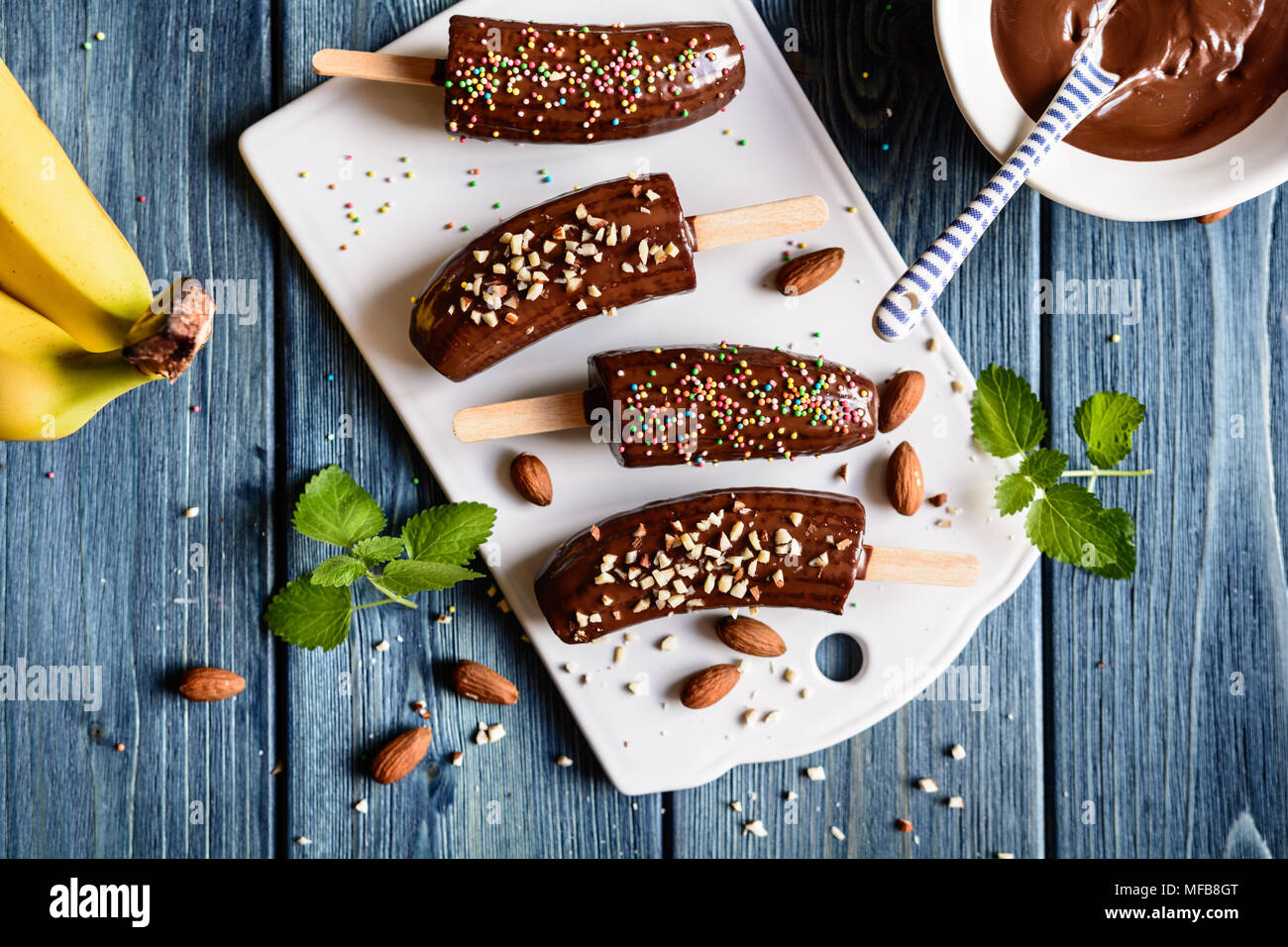 Frische Bananen, umhüllt mit Schokolade und sprengte mit gehackten Mandeln und bunten Streuseln Stockfoto