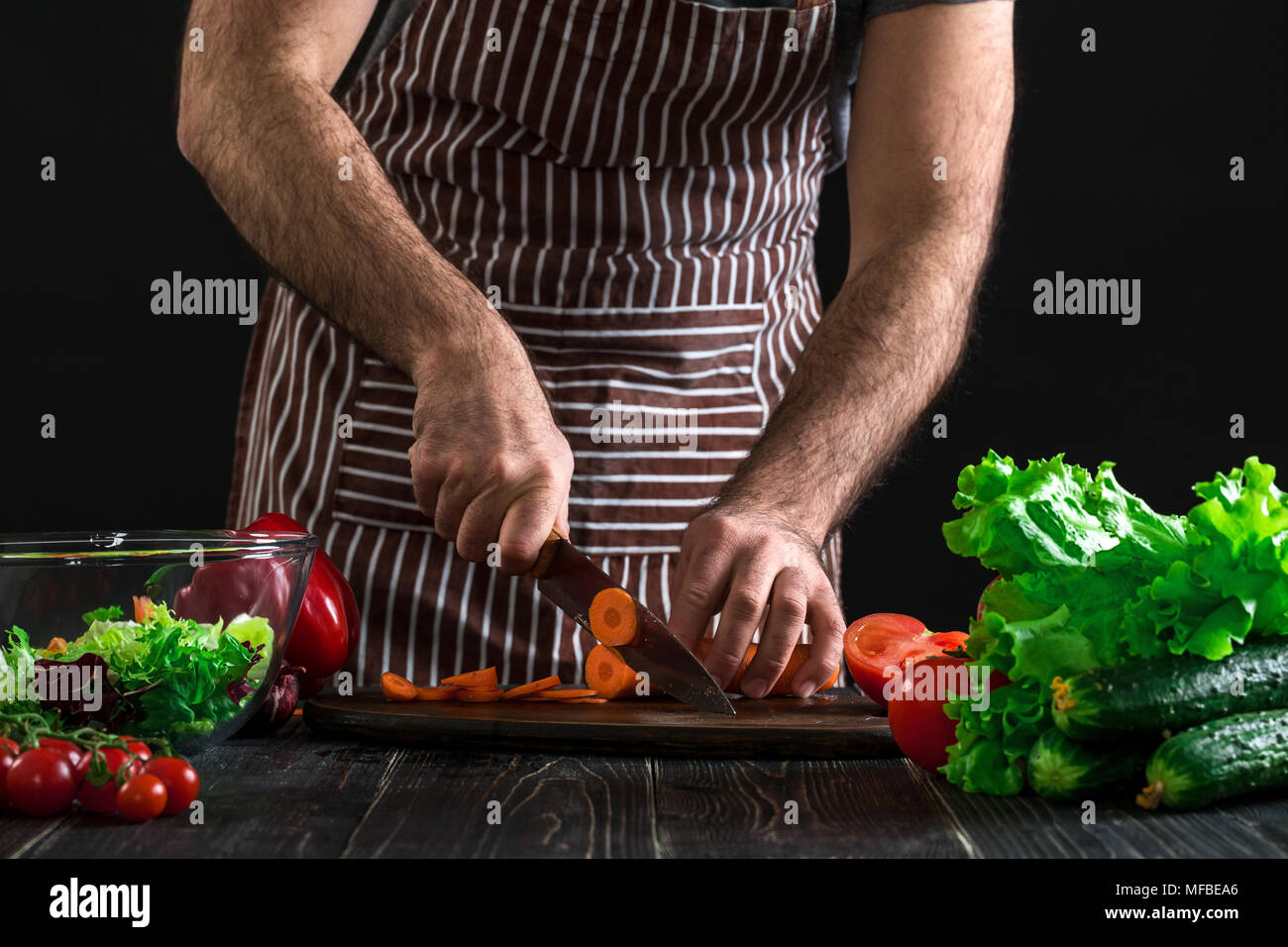 Jungen home cook Mann im Vorfeld schneiden Möhre mit Küchenmesser. Stockfoto