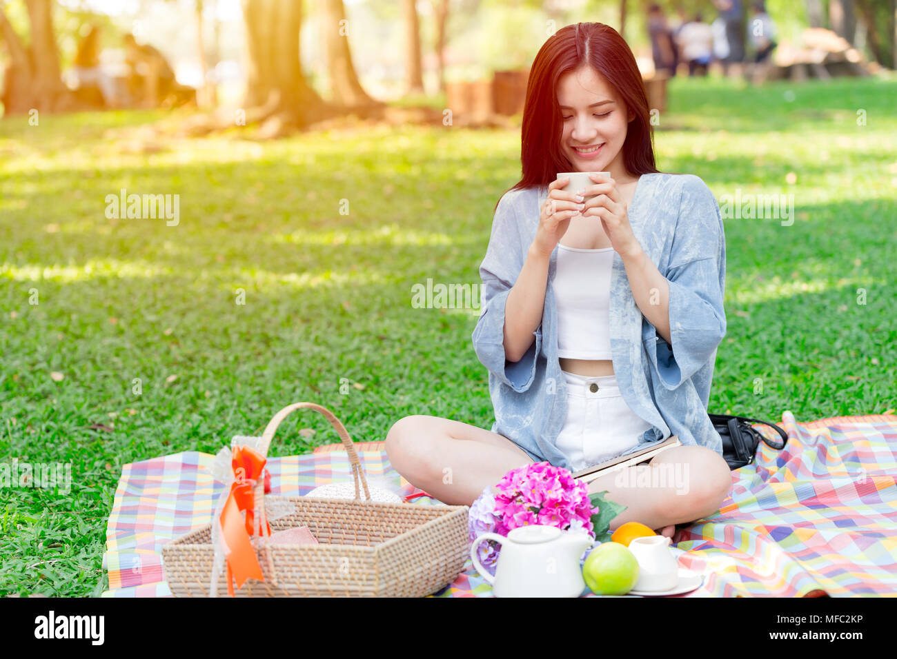 Schöne asiatische Frau mit Becher trinken im Park beim Picknick im Park im Urlaub Stockfoto