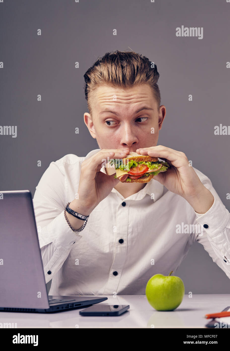 Man Hamburger im Büro Essen, während Video auf seinem Laptop Stockfoto