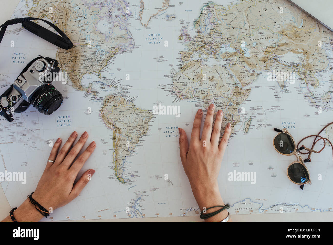 Persönliche Perspektive der weiblichen Touristen auf der Suche auf einer Weltkarte für Planung Urlaub mit einer Kamera und Sonnenbrillen um. Reisende, die eine Reise planen Stockfoto