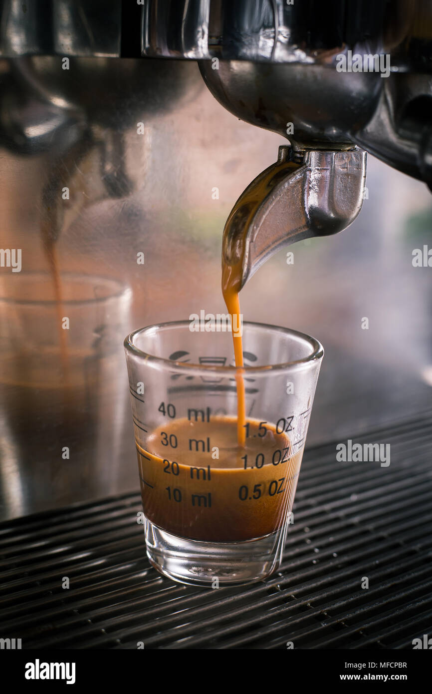 Professionelle Espressomaschine gießen starke suchen frischen Kaffee in eine Maßnahme Glas Schale Stockfoto