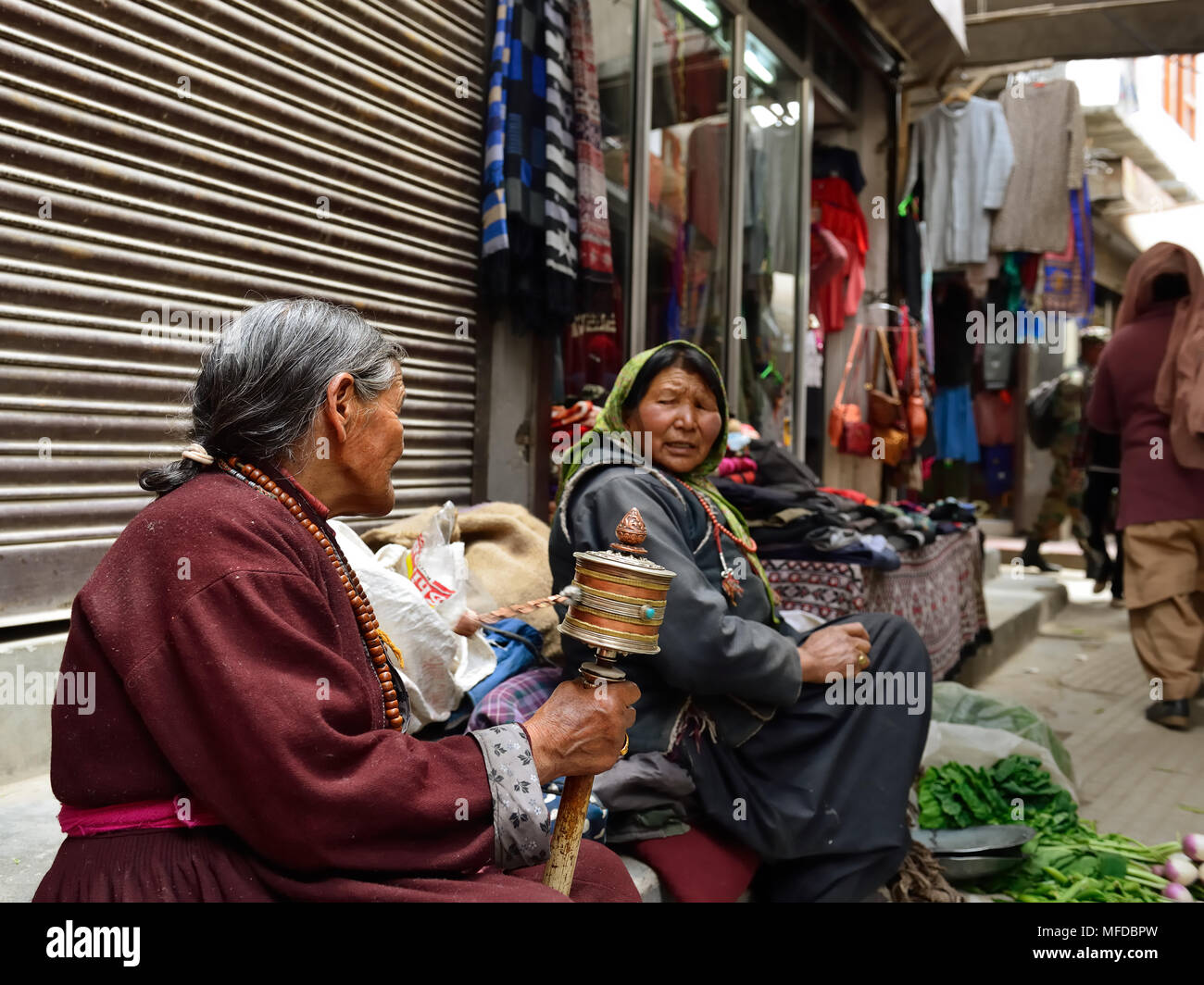 TIBET, Leh, Ladakh, INDIEN - 03 JULI 2017: Buddhistische Frau Gemüse verkaufen in Leh Straßen mit der Tibetischen Gebets Schleifmaschine in der Hand Stockfoto