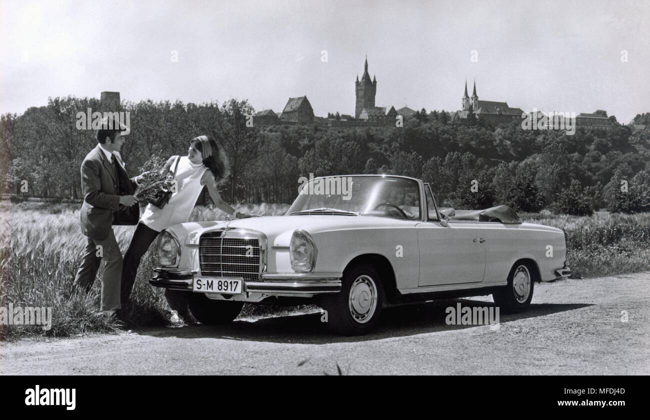 Ein junges Paar im Gras posiert neben einem Mercedes Benz 280 SE 3.5 Cabrio. (Aufnahme von 1969). | Verwendung weltweit Stockfoto