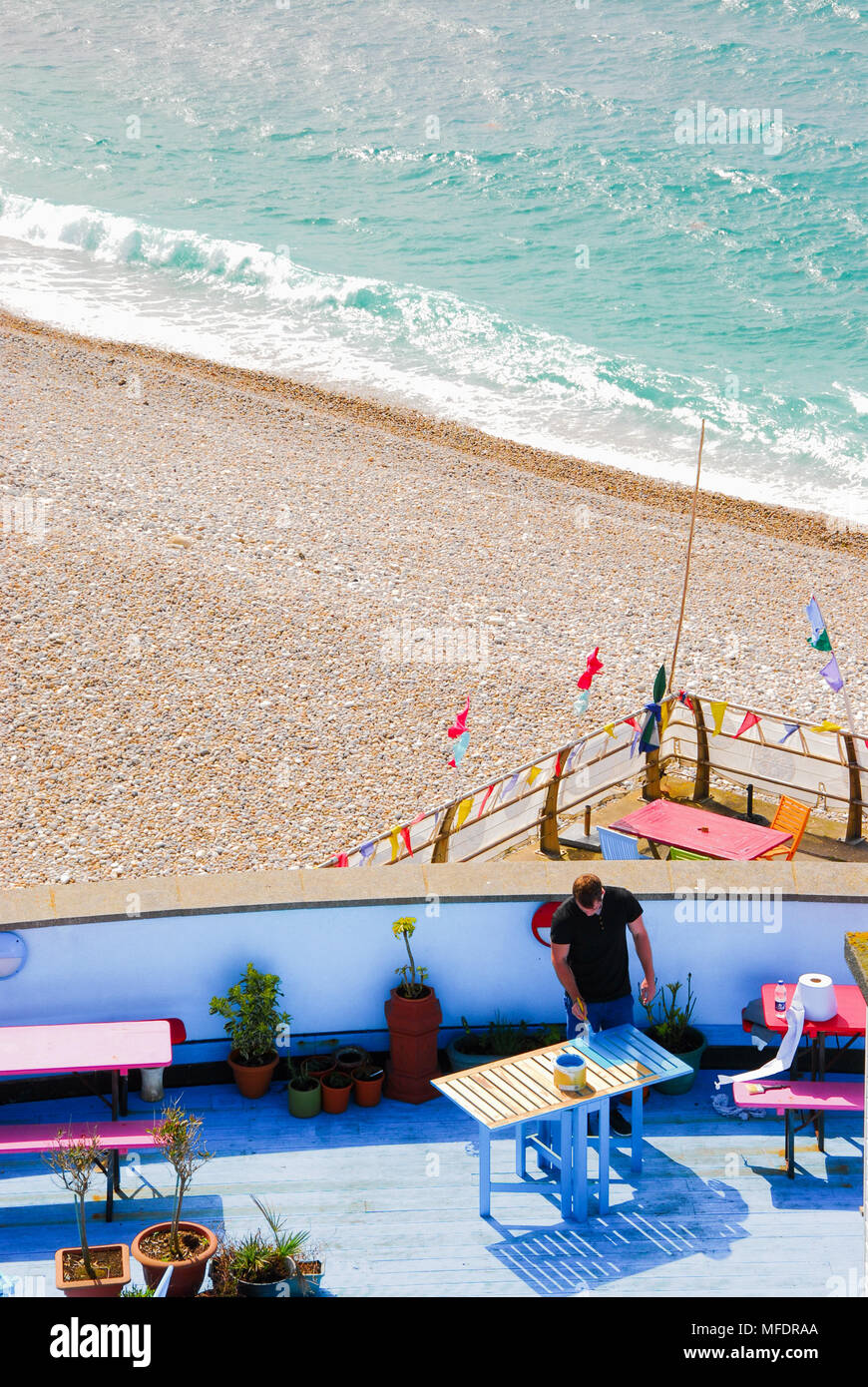Portland. 25. April 2018. UK Wetter: Ein Arbeiter Farben Möbel in der Sonne an einem Chesil Beach Cafe, auf der Isle of Portland Credit: stuart Hartmut Ost/Alamy leben Nachrichten Stockfoto
