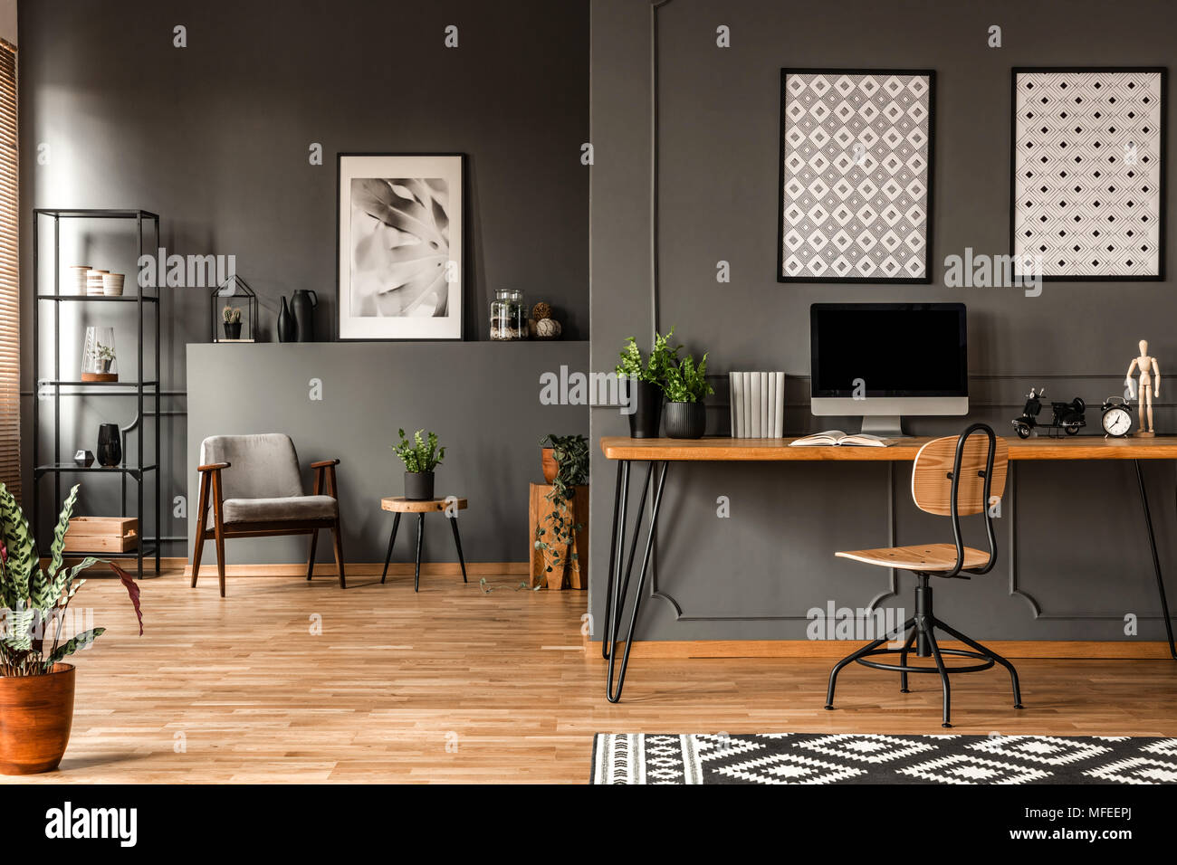 Gemusterte Poster über dem Schreibtisch mit computer monitor Grau home office Einrichtung mit Pflanzen Stockfoto