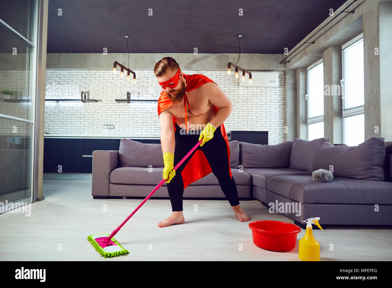 Ein fettes, lustige Mann in einen Superhelden Kostüm ist Reinigung des Hauses. Stockfoto
