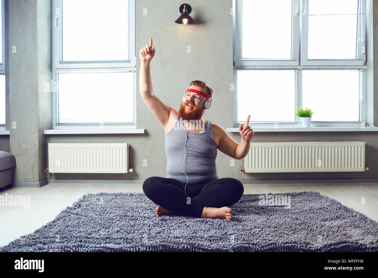 Eine lustige Fetten bärtigen Mann in der Kopfhörer funktioniert Yoga im Zimmer. Stockfoto