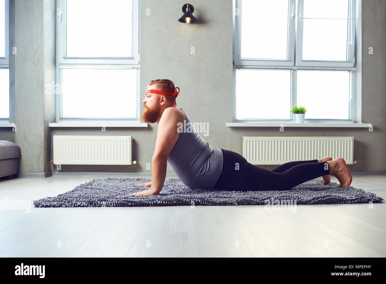 Eine lustige Fetten bärtigen Mann im Sport Kleidung Yoga im Zimmer. Stockfoto