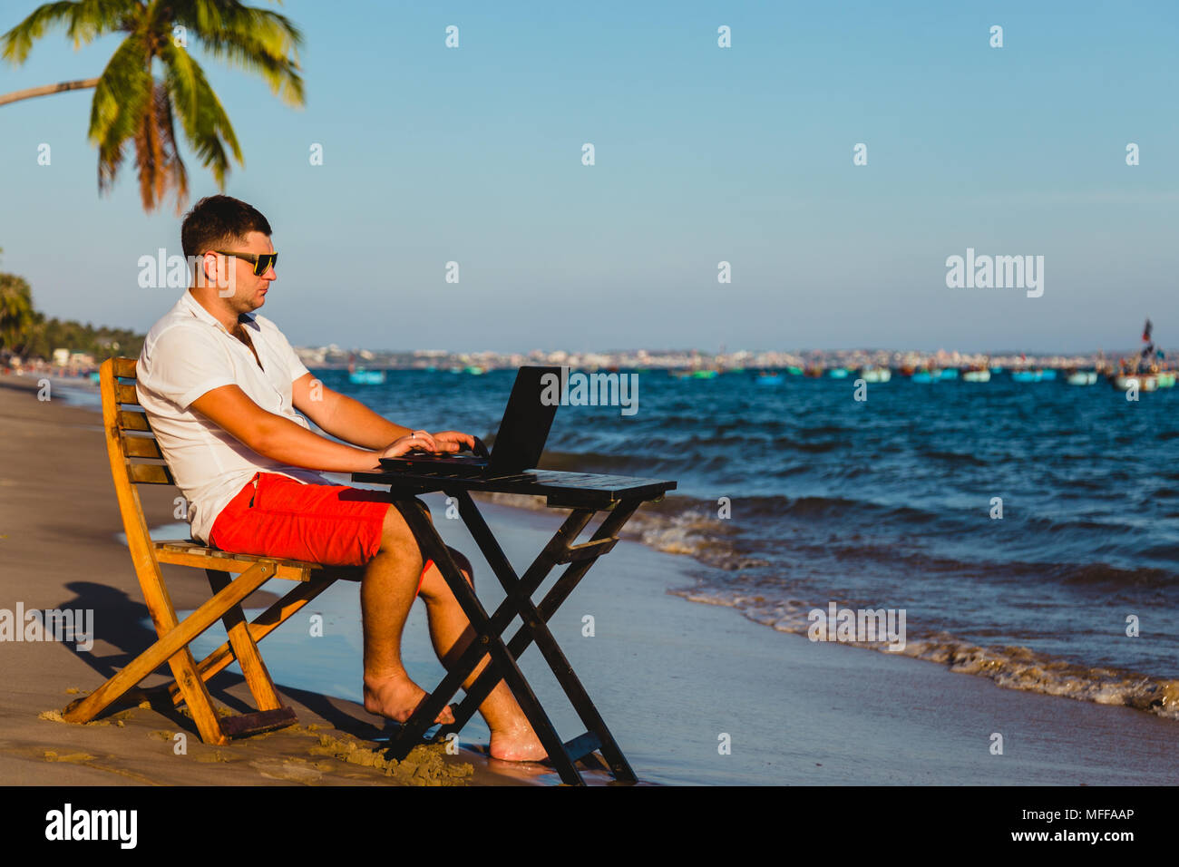 Mann bei der Arbeit mit einem Laptop, auf einer Hängematte am Strand. Konzept der digitale Nomade, externe Mitarbeiter, unabhängige Position Unternehmer. Stockfoto