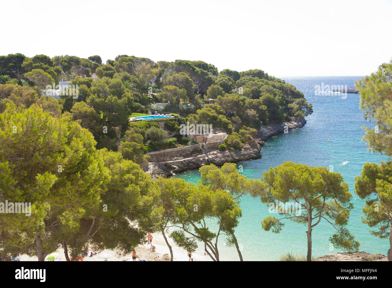 Cala d'Or, Mallorca, Spanien - August 2016 - ein Blick auf den Strand von Cala d'Or durch ein paar Bäume Stockfoto