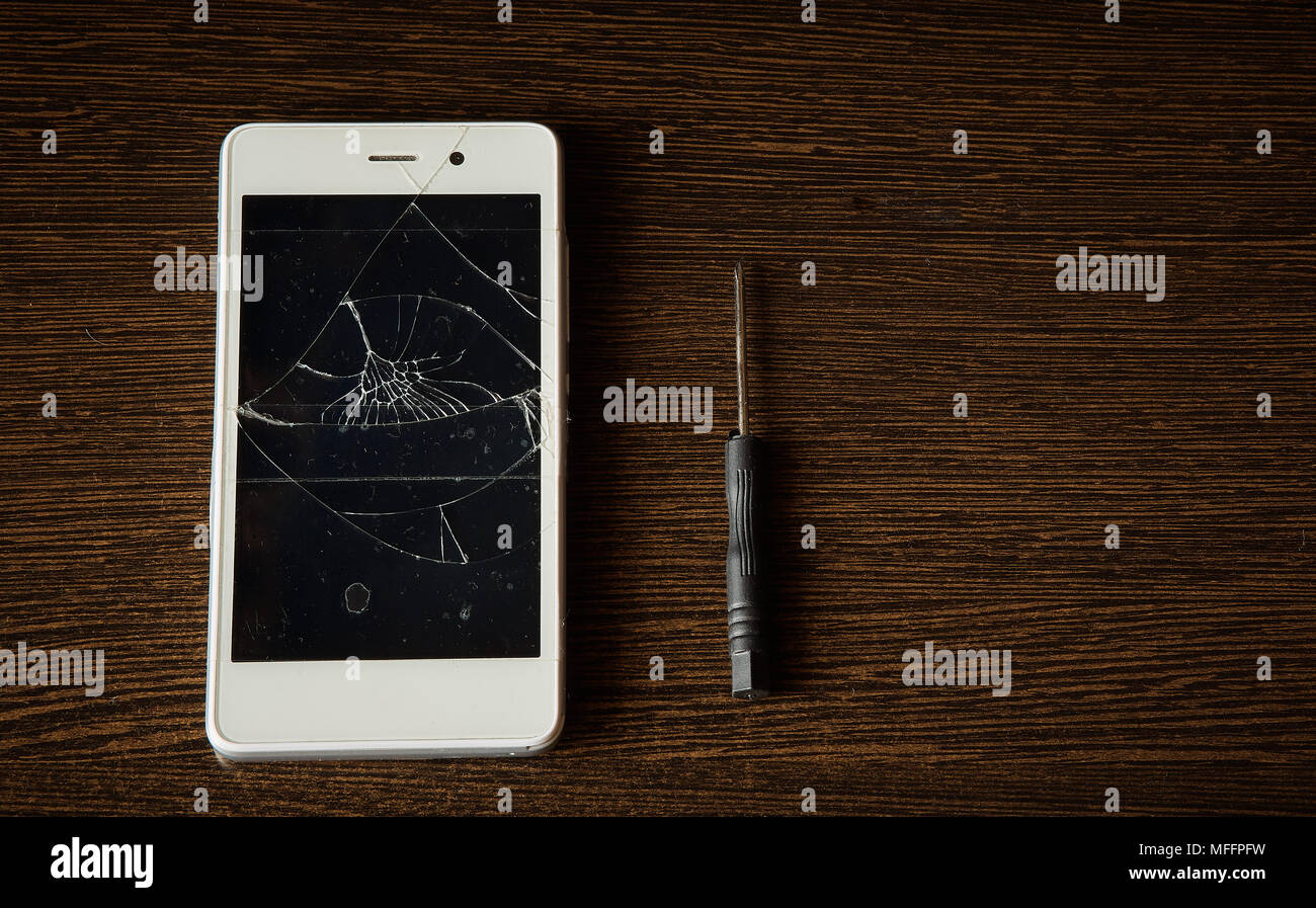 Smart Phone mit defekten Bildschirm auf Holzuntergrund mit kleinem Schraubendreher für Reparatur Stockfoto