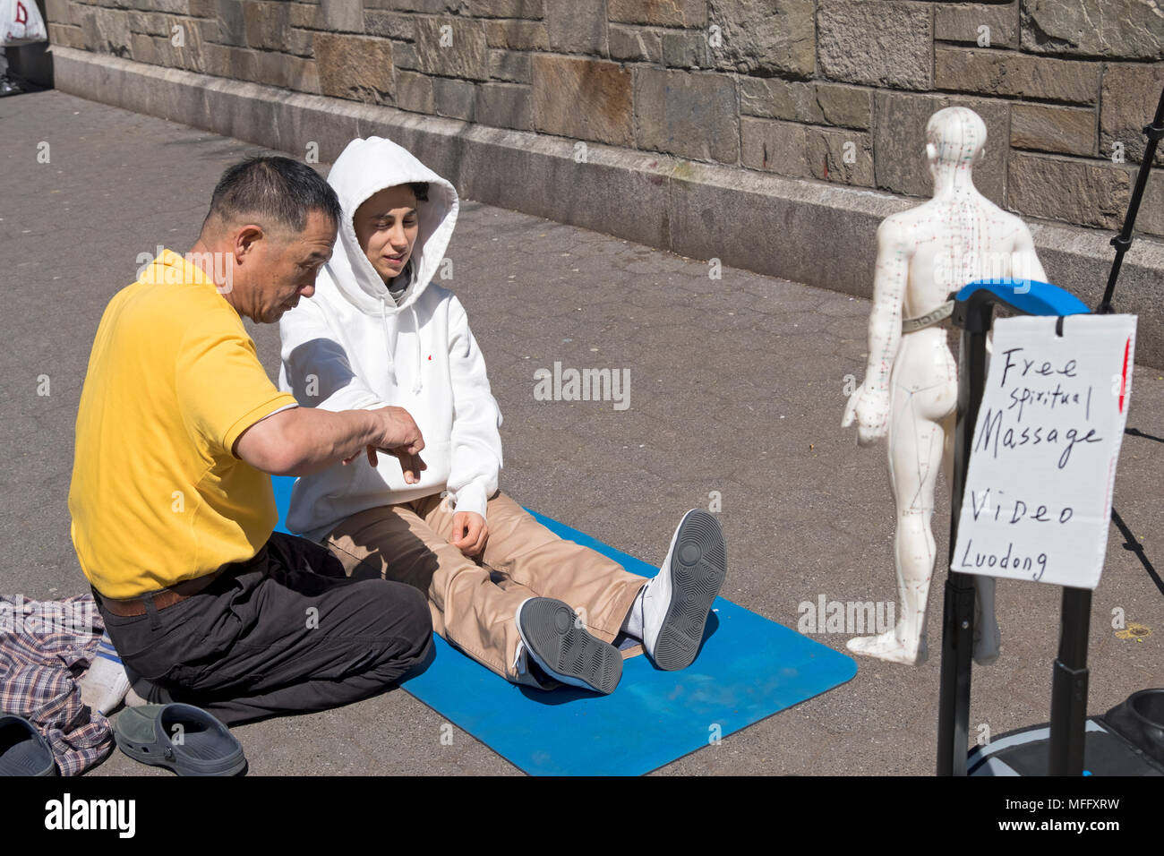 Luo Dong geben eine kostenlose Spirituelle Massage zu einer jungen Dame in einem Kapuzen-sweatshirt. Im Union Square Park, Manhattan, New York City. Stockfoto