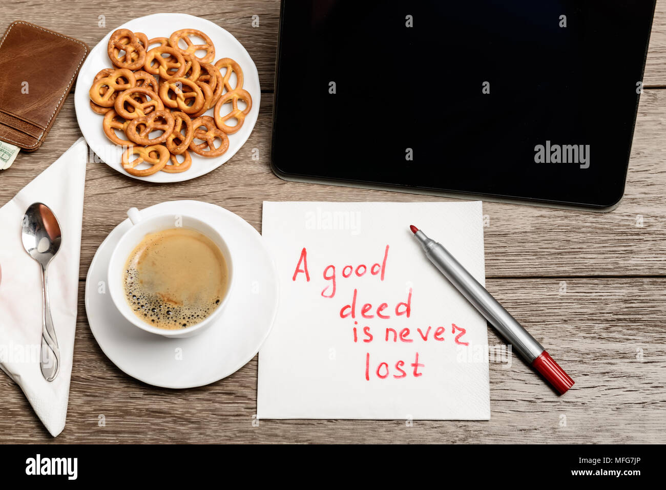 Holztisch mit Kaffee, etwas zu Essen und Serviette Nachricht Sprichwort eine gute Tat nicht verloren geht Stockfoto