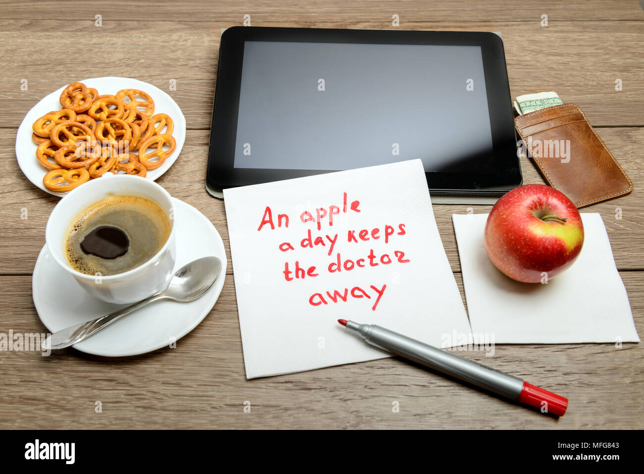 Serviette Handschrift Nachricht Sprichwort auf hölzernen Tisch mit Kaffee, etwas zu Essen und Tablet PC Ein Apfel am Tag hält den Doktor Away Stockfoto