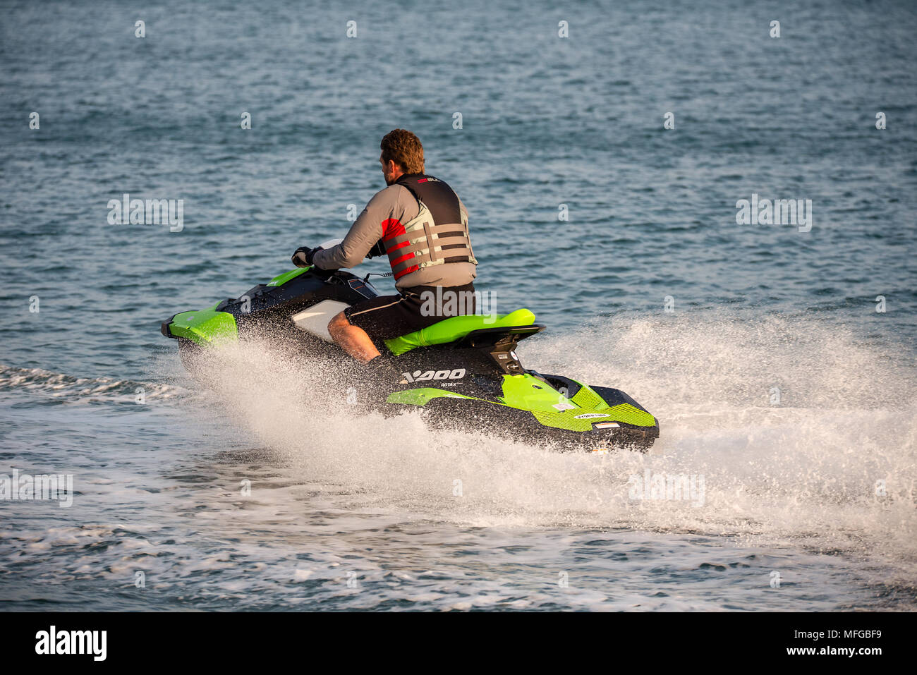 Im mittleren Alter Mann das Tragen einer Schwimmweste reitet eine persönliche Wasserfahrzeuge Jet Ski entlang einer ruhigen Meer. Stockfoto