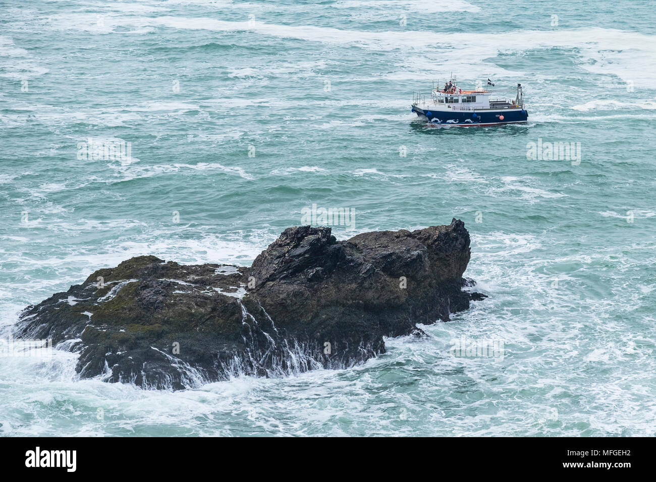 Ein Schiff segeln vorbei an einer kleinen felsigen Insel im Meer vor der Küste von North Cornwall. Stockfoto
