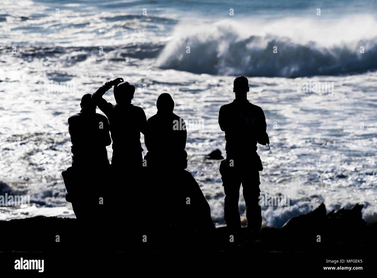 Die Silhouette einer Gruppe von Menschen an der Küste von North Cornwall beobachten große eingehende Wellen. Stockfoto