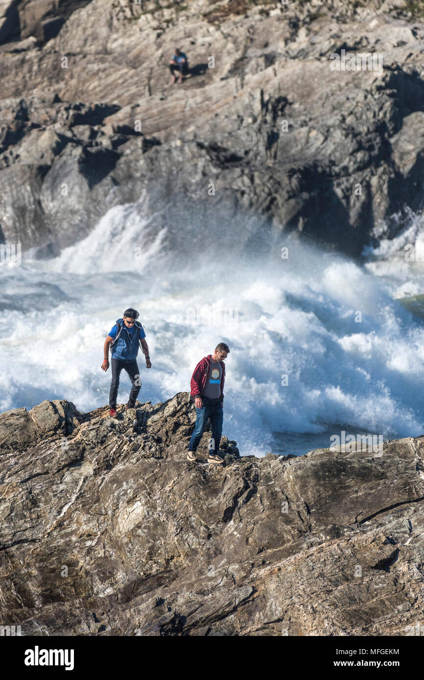 Urlauber setzen sich an der Gefahr zu Fuß über die Felsen wie große Wellen brechen am Ufer. Stockfoto