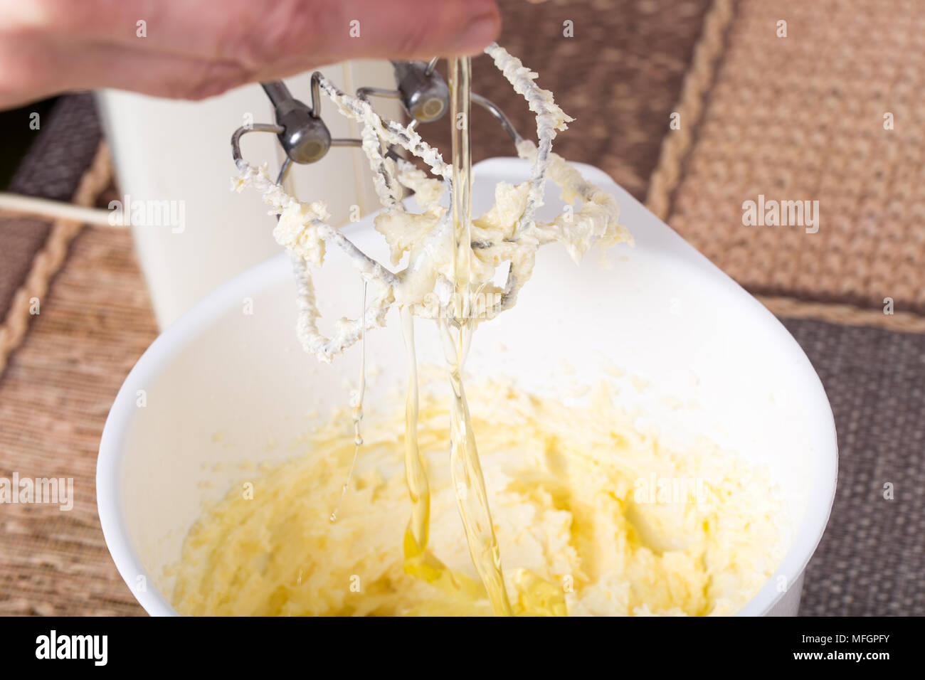 Hinzufügen von hühnerei auf die Butter für die Herstellung von Kuchen in Weiß mixer Schüssel auf eine Tabelle als Hintergrund. Stockfoto