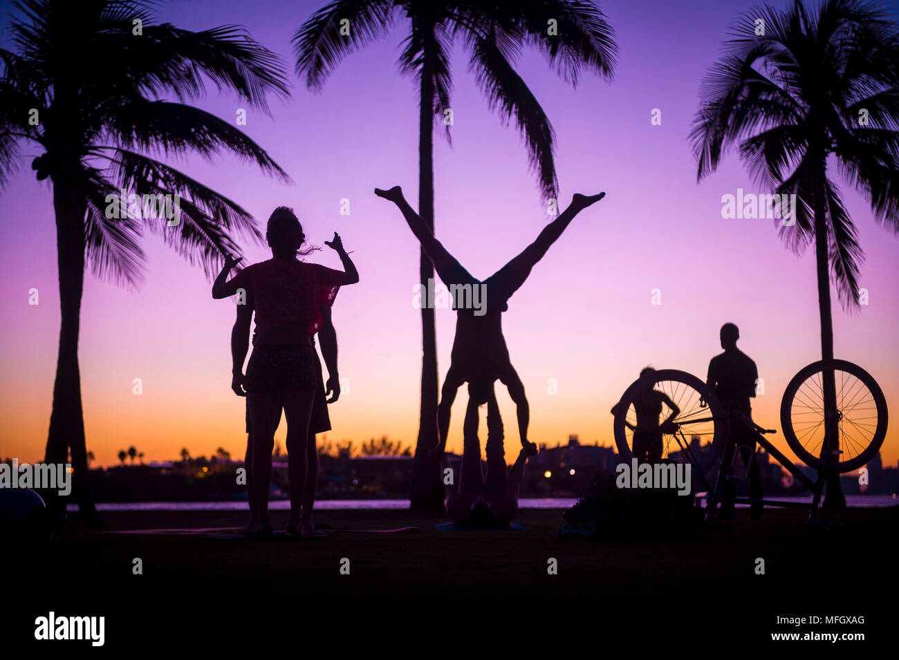Silhouetten der unkenntlich Menschen üben Yoga unter Palmen bei Sonnenuntergang Stockfoto