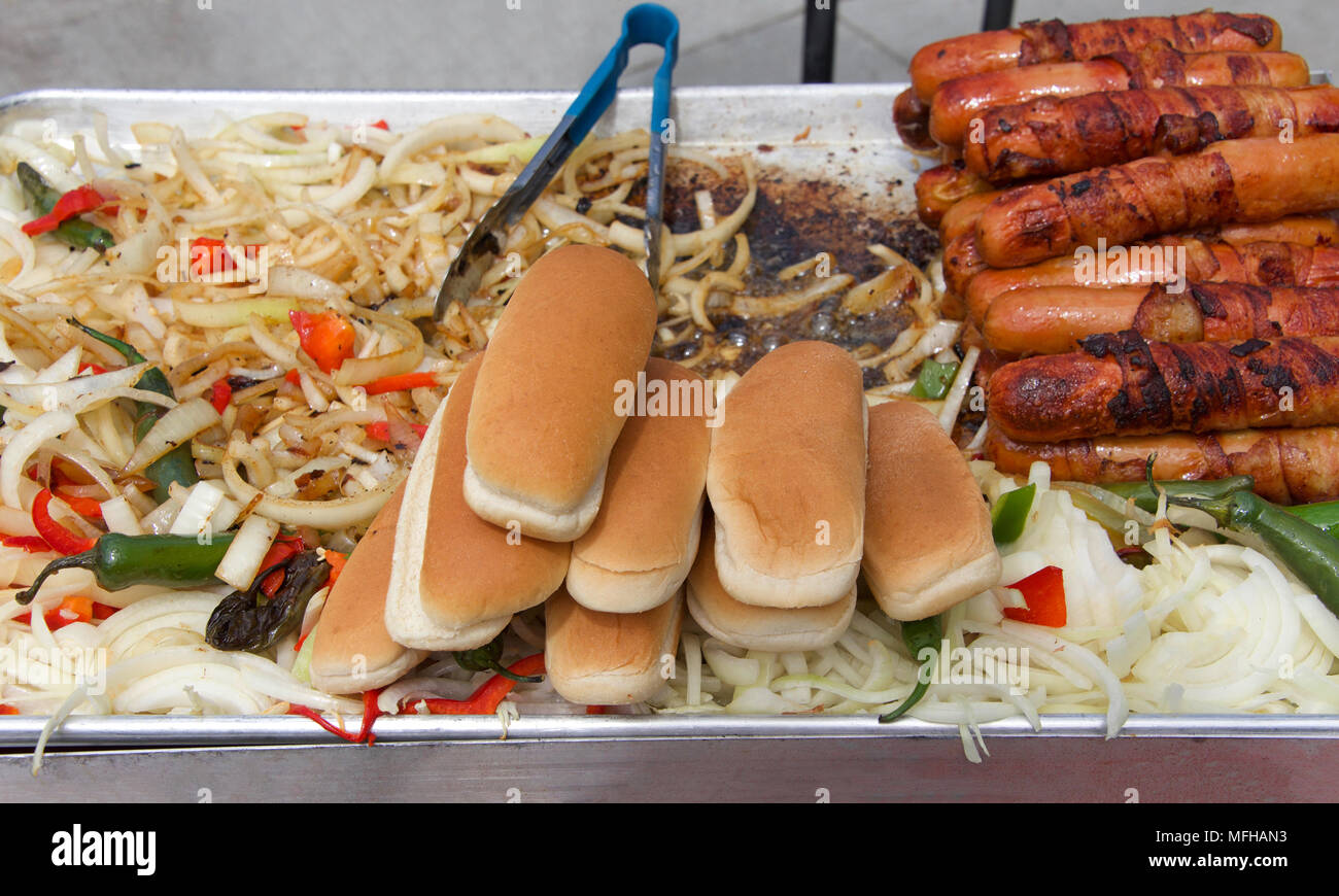 Hot dog street Hersteller Grill mit Speck umwickelt Hot Dogs, Zwiebeln, Pfeffer, Jalapenos auf eine dampfende Grill mit Zangen in Hintergrund und Hot Dog Buns. Pop Stockfoto