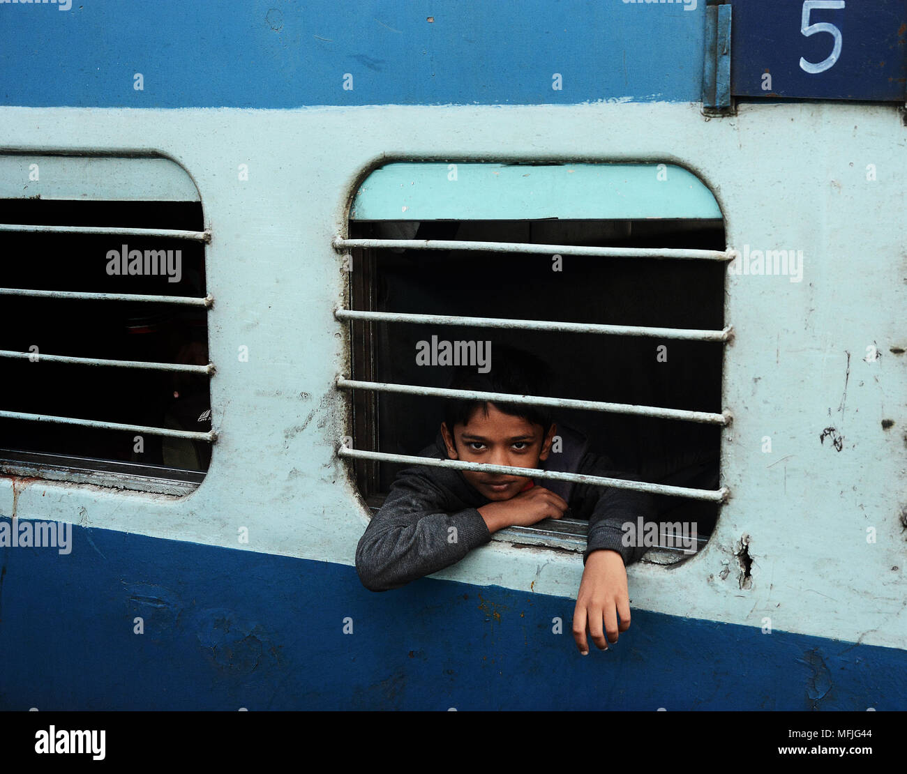 Ein Junge peering aus dem vergitterten Fenster eines vorbeifahrenden Zuges, Indien Stockfoto