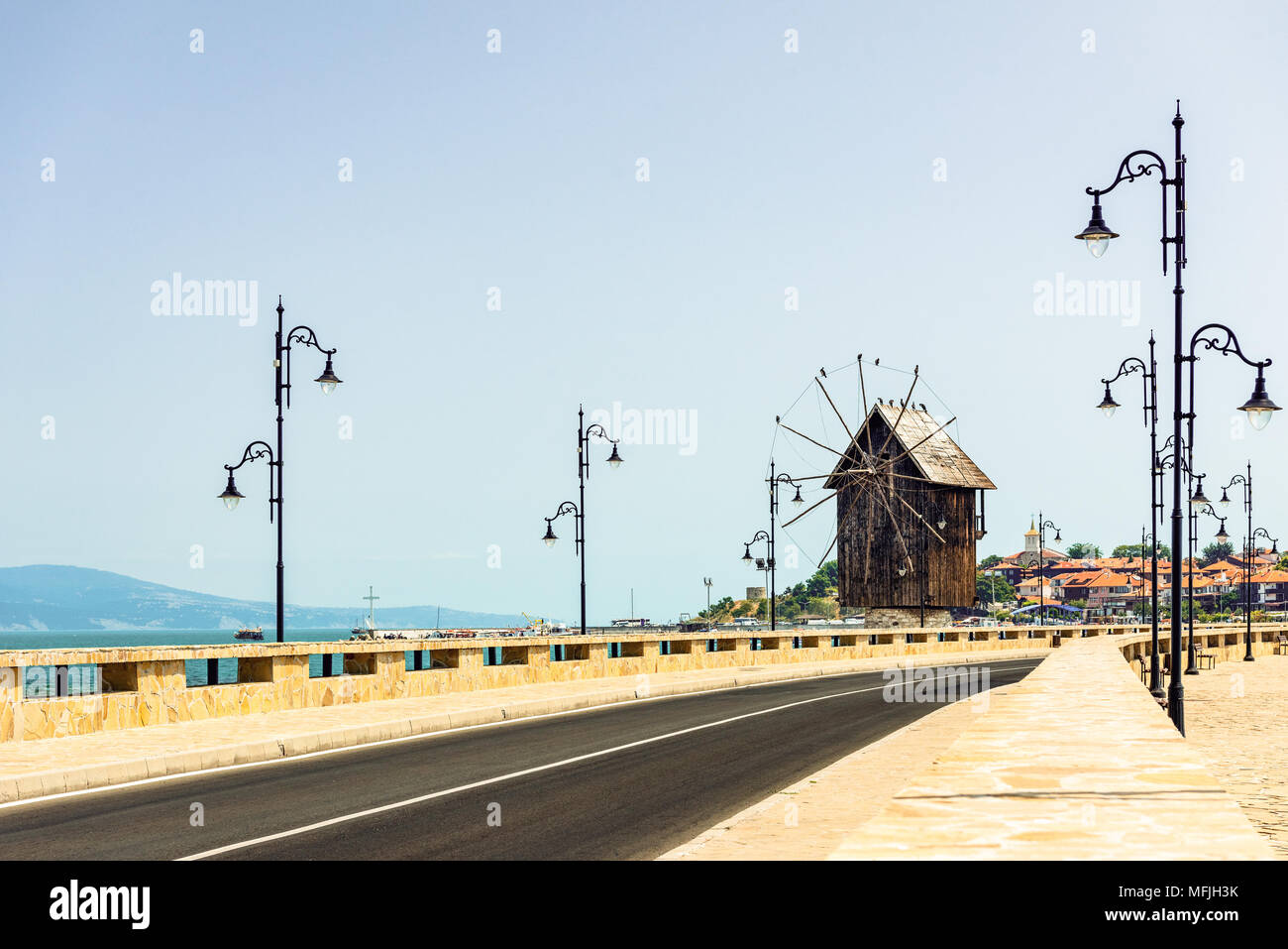Nessebar, Bulgarien - leere Straße mit alten Straßenlaternen und hölzerne Windmühle am Isthmus von Nessebar in hellen, sonnigen Tag, dem Schwarzen Meer im Hintergrund Stockfoto